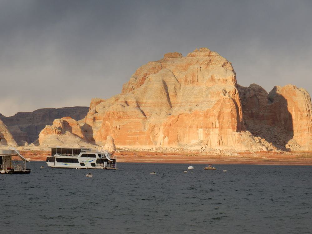 Sunset lights up the rocks on lake Powell. Lots of boats sit in the bay.